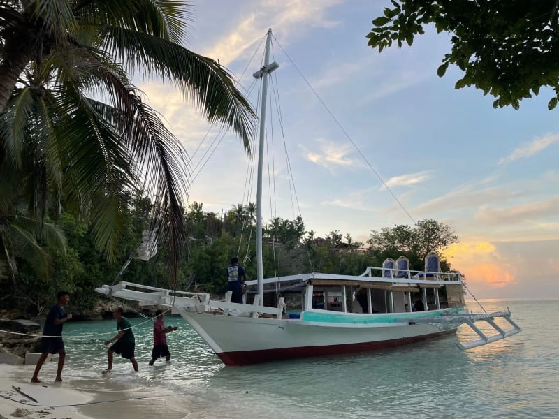 Crew bringing a white phinisi onto a palm-fringed beach at dusk
