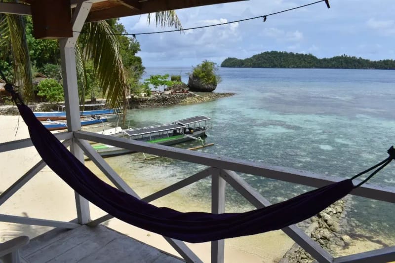 A hammock on a beach bungalow veranda overlooking a reef and a small island